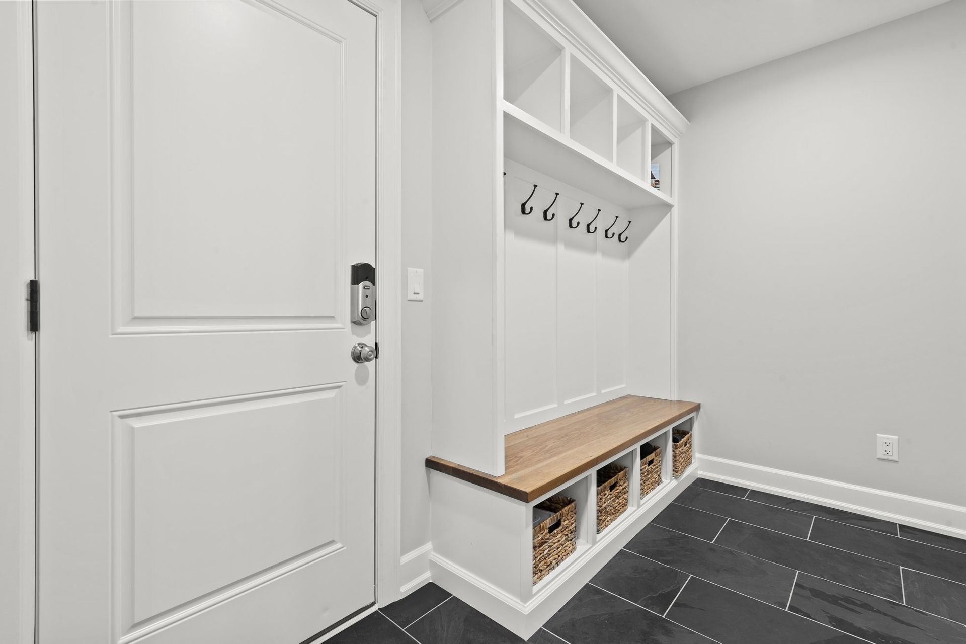 Mudroom with a white built-in locker bench, coat hooks, storage baskets, and a dark tile floor.