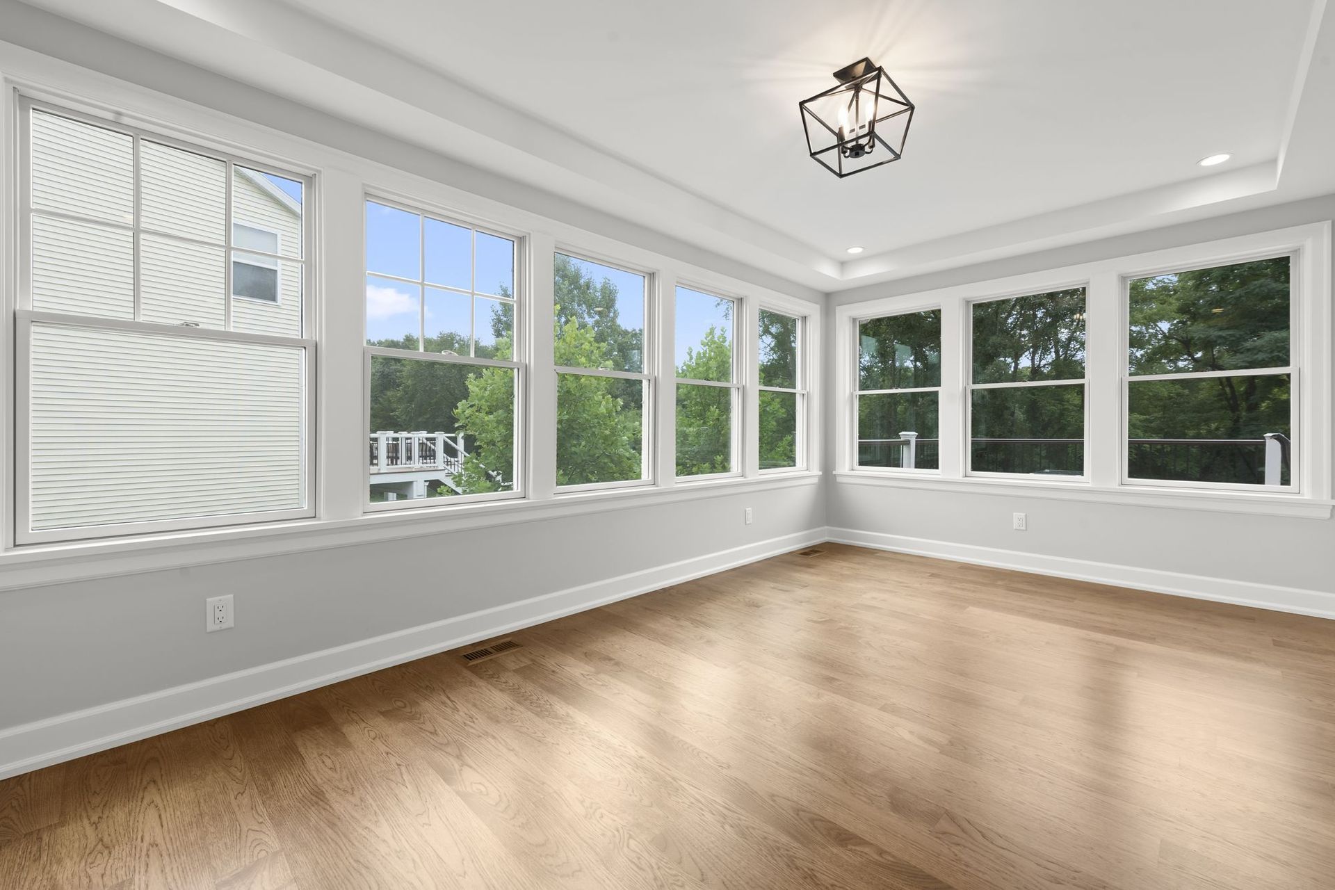 Sunroom addition with windows on two walls, a tray ceiling, and hardwood floors.
