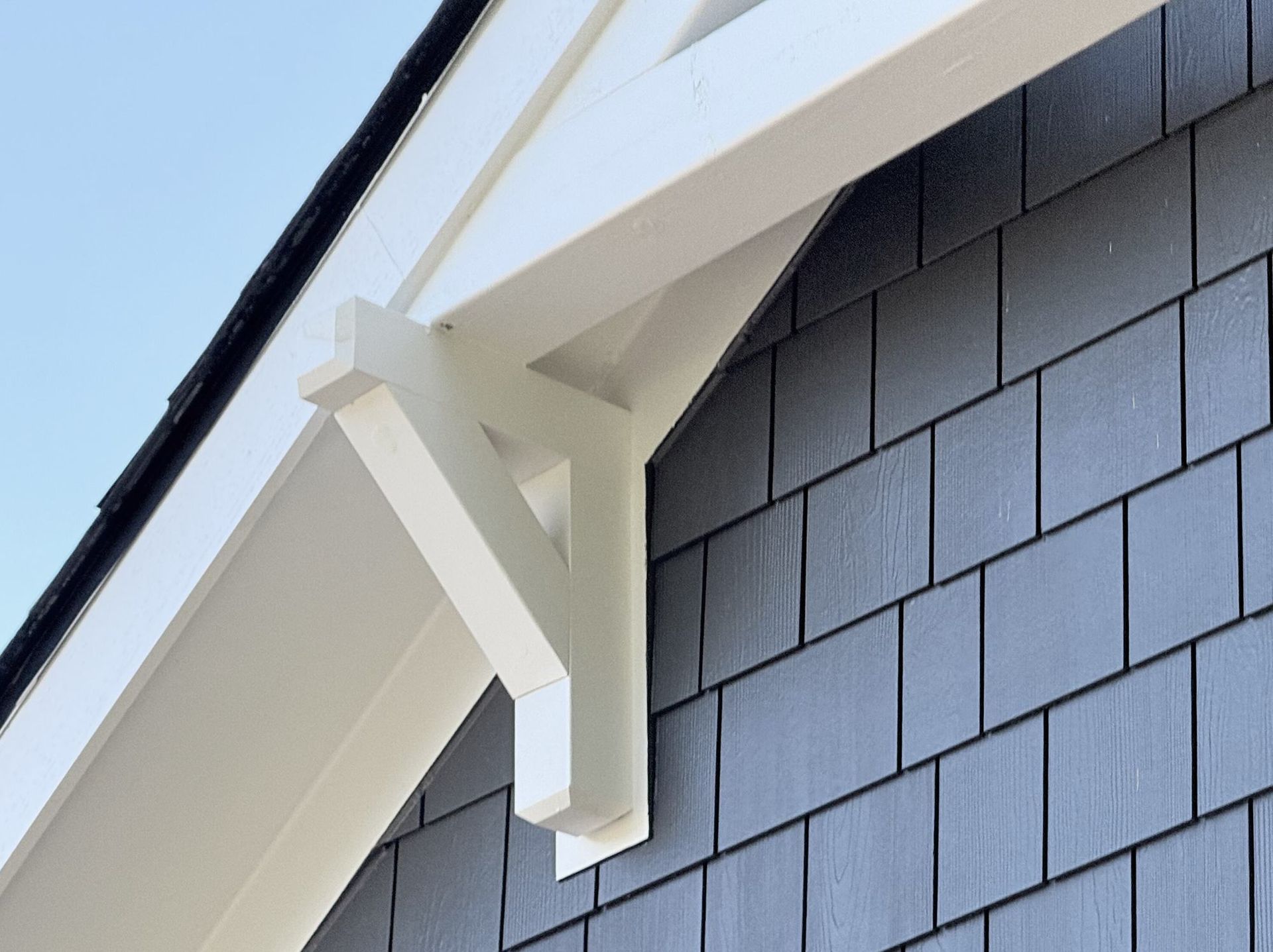 Custom cedar bracket painted white under a gable with Hardie shingle siding.