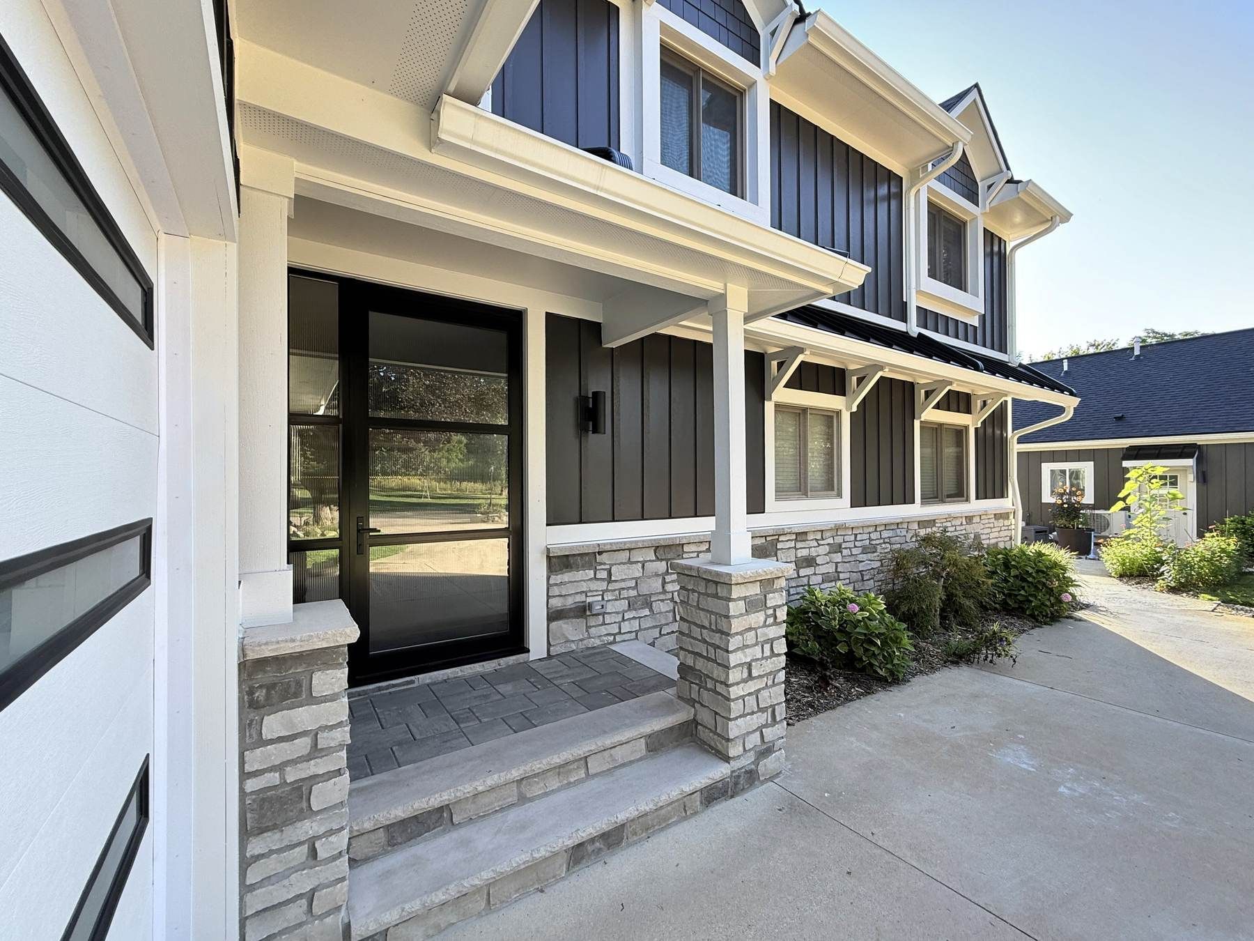 New front porch with natural stone column bases, white posts, a black glass front door, and paver steps.