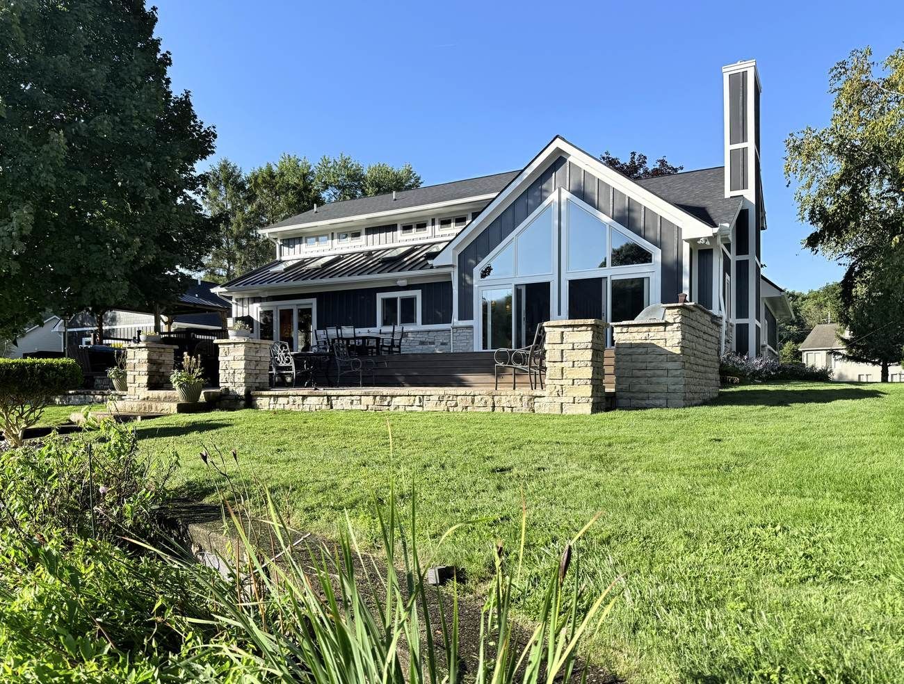 Lake side of the house with a tall gable of angled windows and glass doors, dark board and batten siding, and white trim.