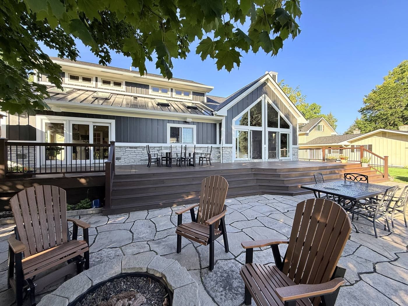 Back of the house with a standing seam metal roof, skylights, white-trimmed doors, and stone along the base above the deck.