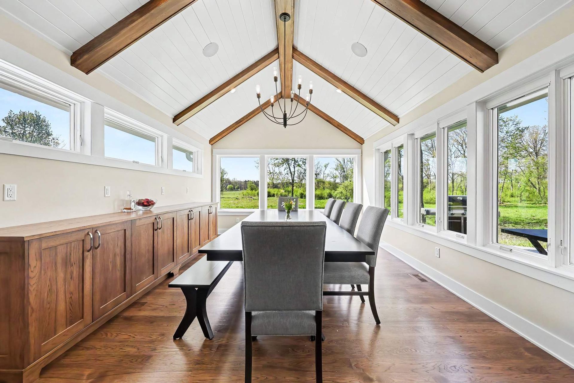 Dining room addition with a vaulted painted shiplap ceiling, stained hickory beams, custom wood cabinetry, and a window wall facing a wetland.