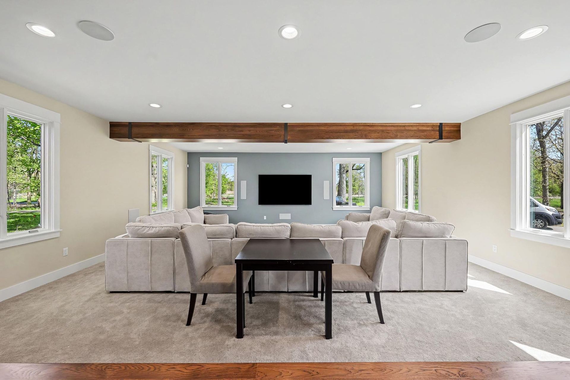 Media room in a converted garage with a cedar wrapped ceiling beam, carpet for acoustics, wall-mounted television, and a large sectional sofa.