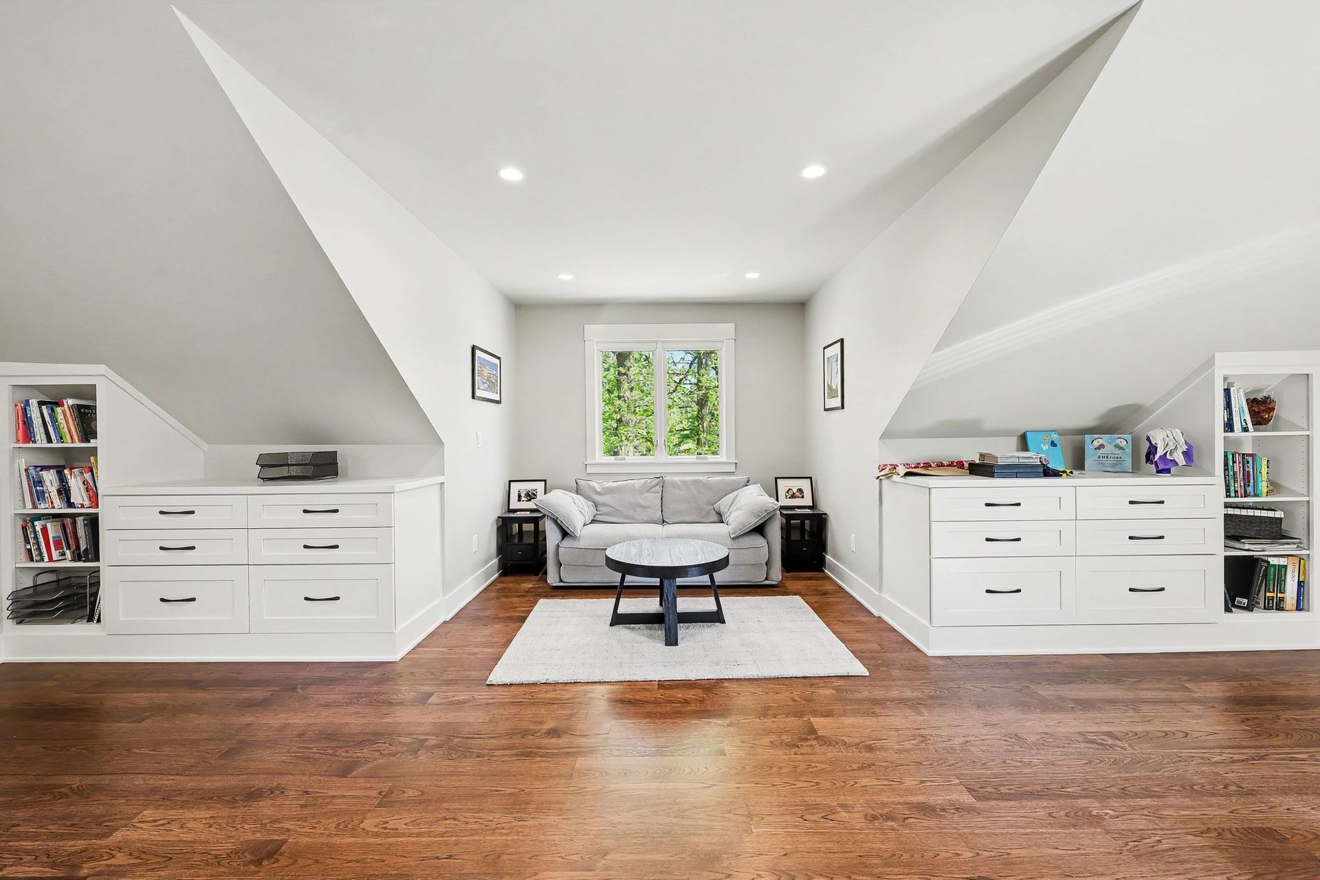 Upstairs office built into a reframed attic, with white drawer banks and bookcases set into the dormer knee walls and hardwood floors.