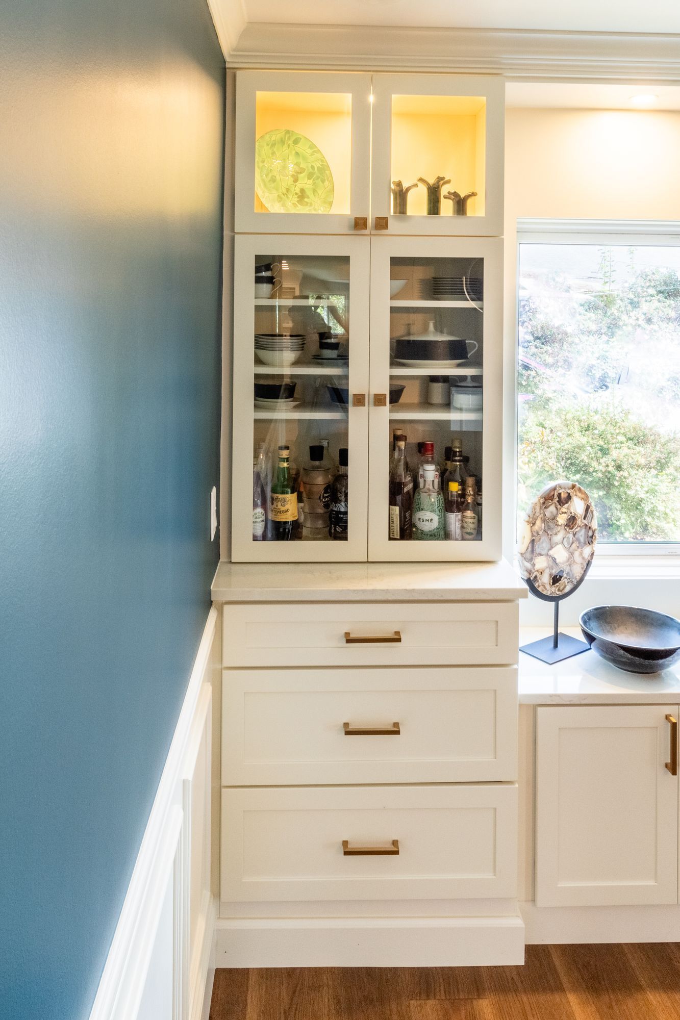 Built-in dining room cabinet with lit glass-front uppers and drawers below a white quartz top.