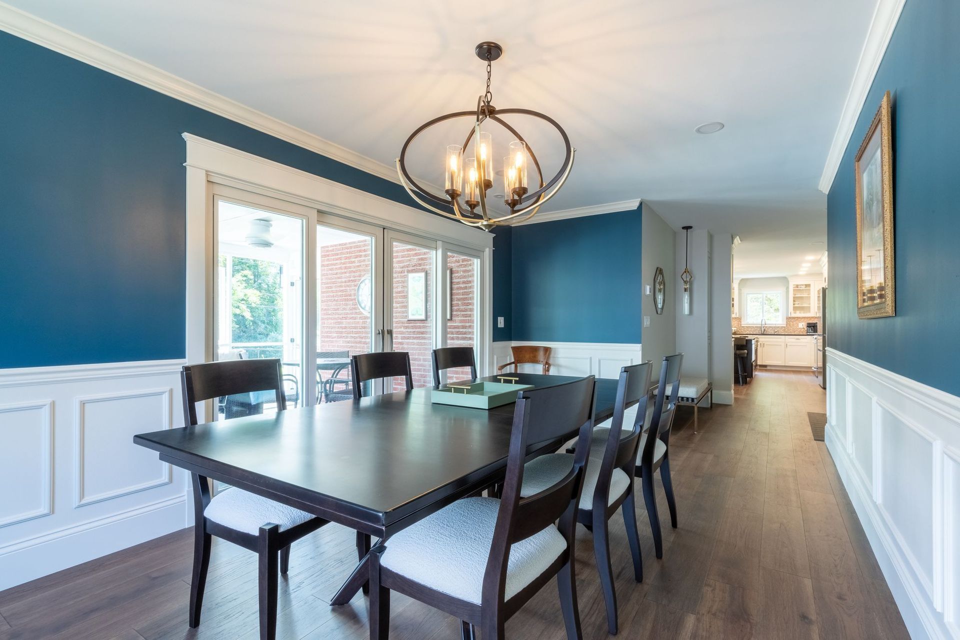 Dining room with deep blue walls, white picture-frame wainscoting, an orb chandelier, and wide sliding doors to a screened porch.