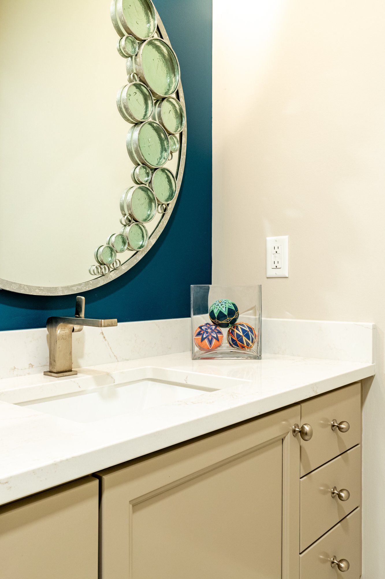Half bath vanity with a painted cabinet, white quartz top, and a round mirror on a deep teal accent wall.