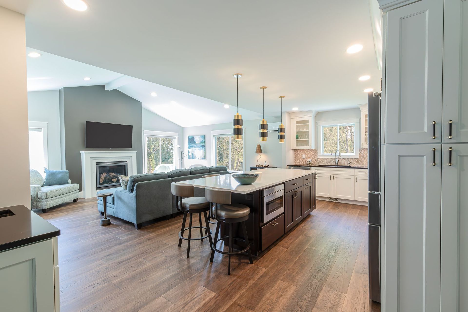 Remodeled kitchen with a dark stained island, white quartz top, and brass pendants, open to a vaulted family room with a gas fireplace.