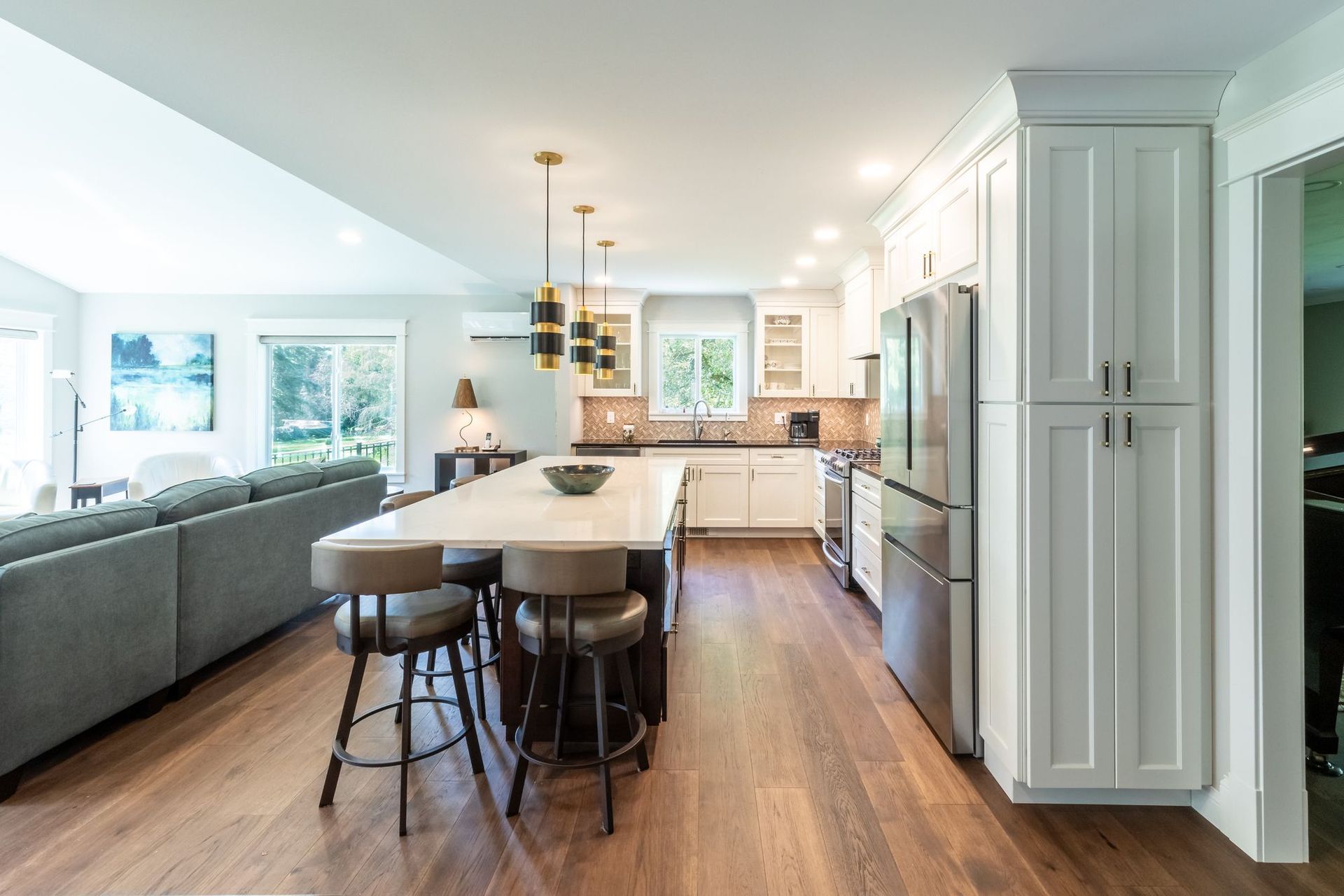 Kitchen island with four stools and a white quartz top, white shaker cabinets to the ceiling, and a tall pantry cabinet.