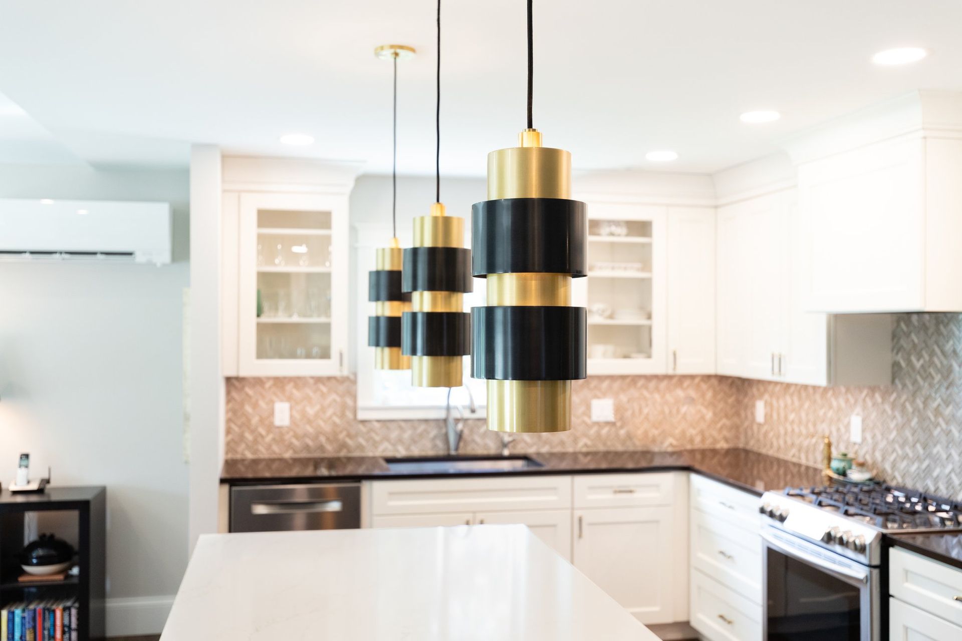 Black and brass cylinder pendant lights over a white quartz kitchen island.