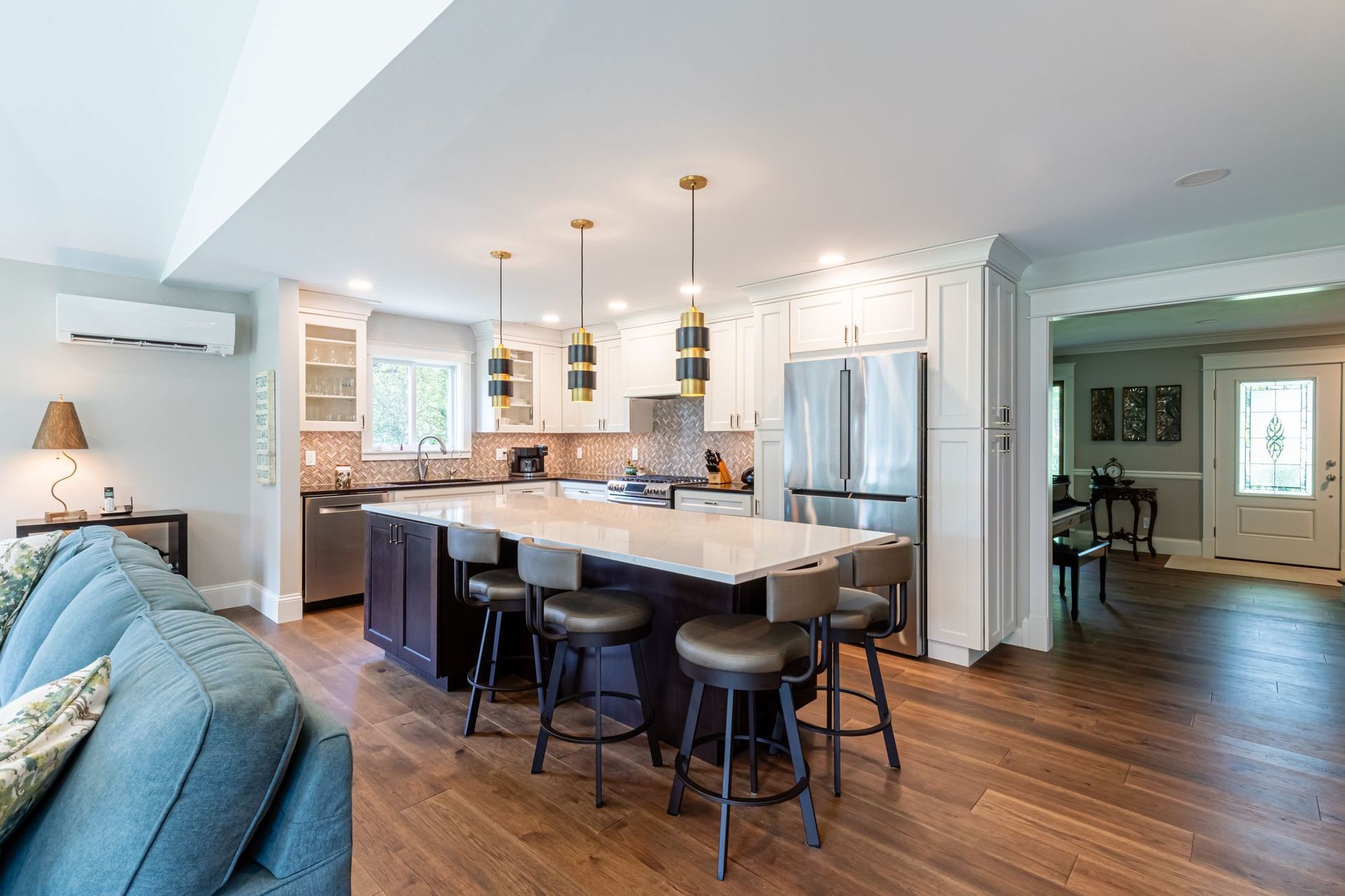 Remodeled kitchen with a dark stained island, white quartz top, and brass pendants, open to a vaulted family room with a gas fireplace.