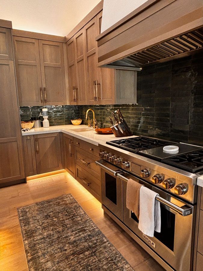 Modern kitchen with wood cabinets, dark tile backsplash, stainless stove, and under-cabinet lighting