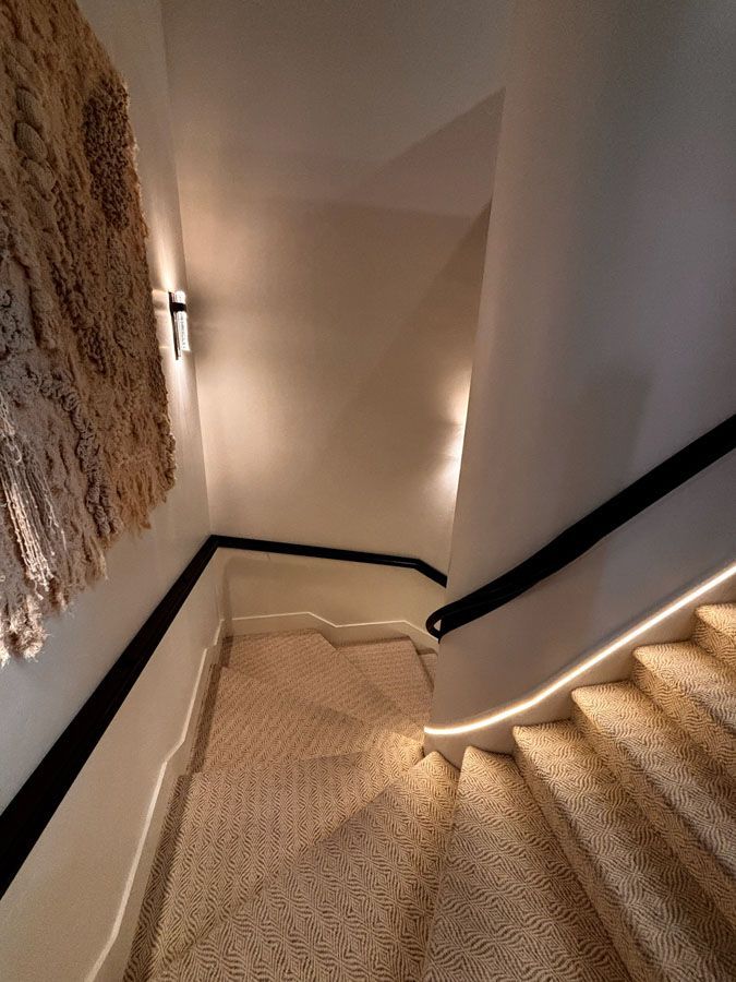 Stairwell with beige carpet, white walls, black trim, and wall sconces on a descending staircase.
