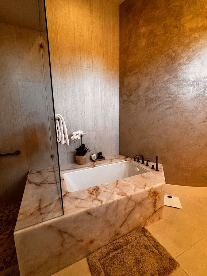 Modern bathroom with marble bathtub surround, beige tile floor, and white flowers on a ledge
