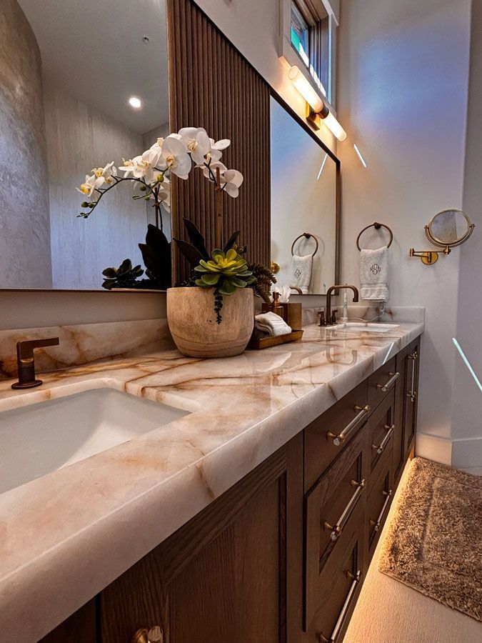 Elegant bathroom vanity with marble countertop, dark wood cabinets, mirror, and orchid decor.
