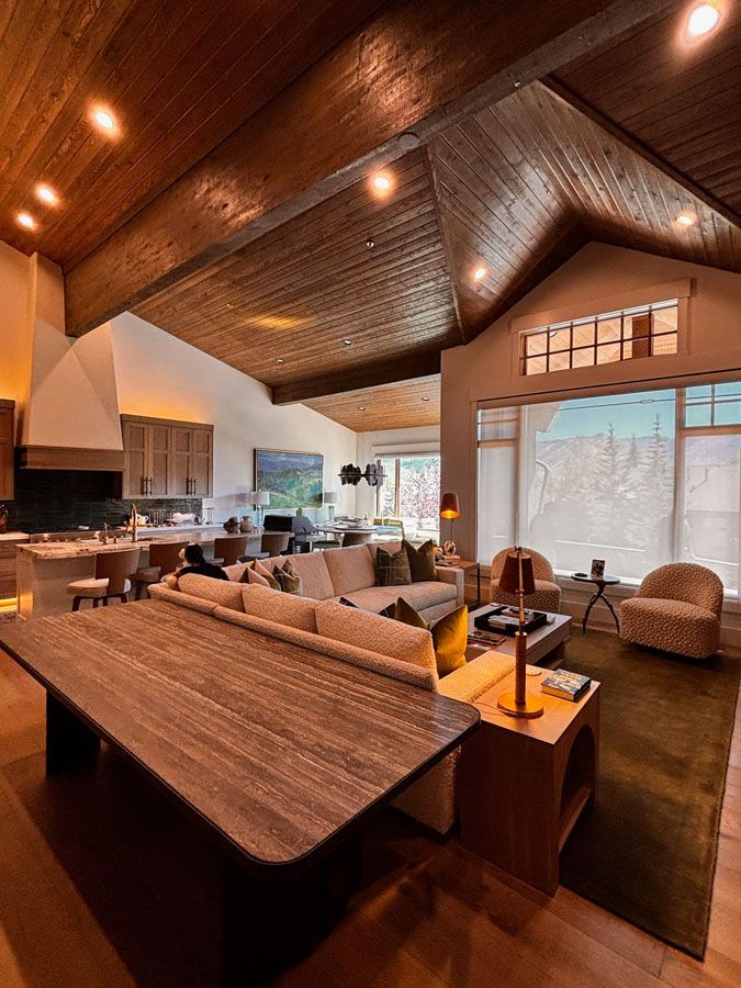 Warm modern living room with vaulted wood ceiling, sectional sofa, and large windows overlooking outdoors