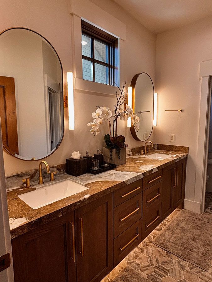 Elegant bathroom vanity with double sinks, round mirrors, wood cabinets, and marble countertop
