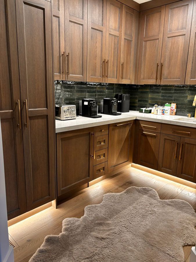 Wood-paneled kitchen corner with black countertop appliances, under-cabinet lighting, and a beige rug.