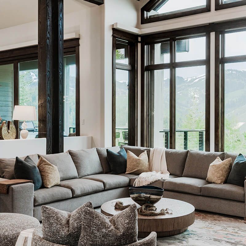 Spacious living room with sectional sofa, round coffee table, and floor-to-ceiling windows with mountain views
