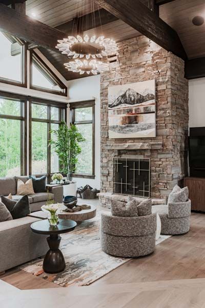 Modern living room with stone fireplace, large windows, and gray seating in a bright, wood-beamed space