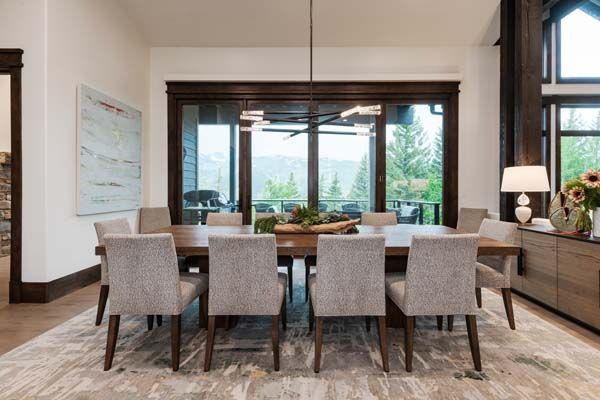 Modern dining room with eight gray chairs, wooden table, large window view, and neutral decor