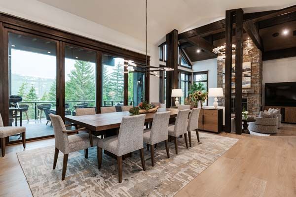 Modern dining room with large windows, wood table, upholstered chairs, and stone fireplace accents