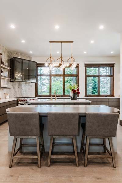 Modern kitchen with gray island, pendant lights, and large windows overlooking greenery