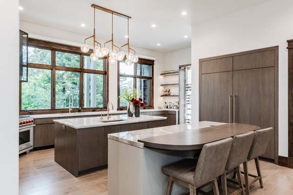 Modern kitchen with large windows, island, pendant lights, and gray chairs beside a dining table