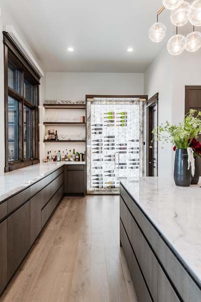 Modern kitchen with marble countertops, wood floors, open shelves, and a glass-door pantry at the end.