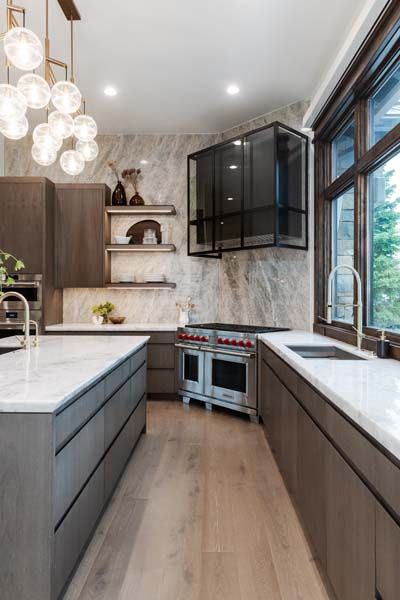 Modern kitchen with dark cabinets, white countertops, and large windows beside a stainless stove.