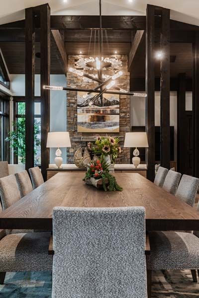 Modern dining room with a long wooden table, upholstered chairs, and a chandelier-lit mirrored wall.