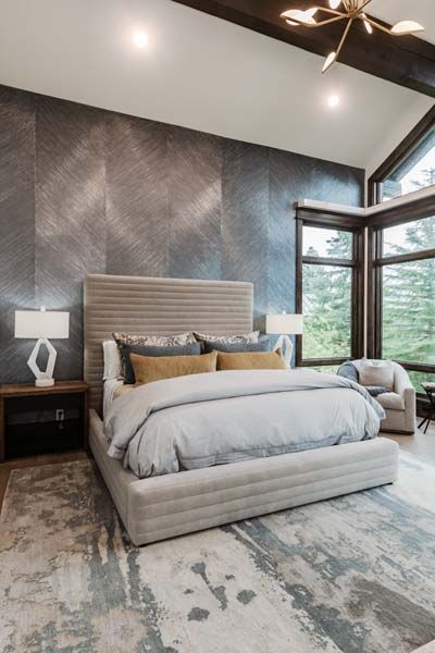 Luxury bedroom with gray upholstered bed, dark accent wall, and large windows overlooking greenery