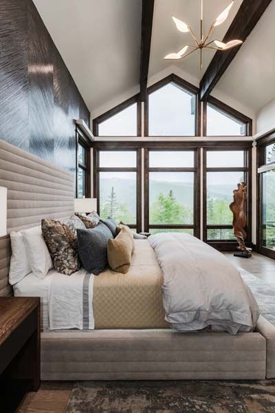 Modern bedroom with vaulted windows, a beige bed, and a view of greenery outside.