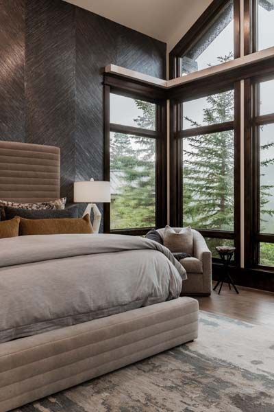 Modern bedroom with large corner windows, gray upholstered bed, and mountain view