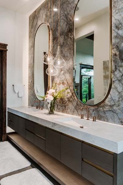 Modern bathroom vanity with marble-look wall, oval mirrors, and a long dark cabinet