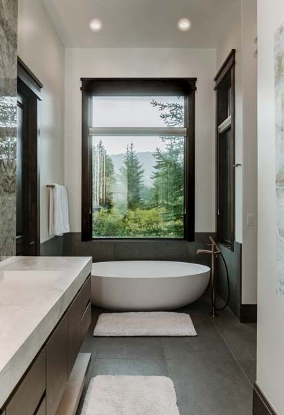Modern bathroom with freestanding tub, large window, and gray stone finishes