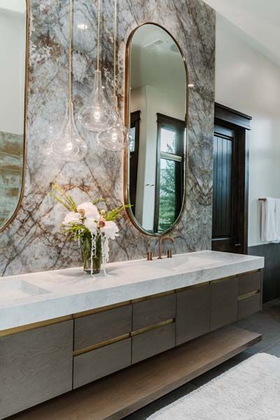 Modern bathroom vanity with marble wall, oval mirror, flowers, and dark wood cabinetry.