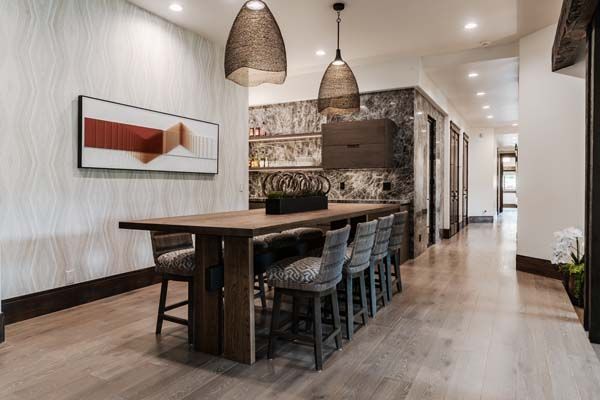 Modern dining room with a long wooden table, woven pendant lights, and patterned wall decor