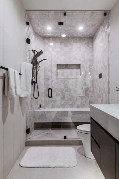 Modern bathroom with glass shower, marble walls, vanity, toilet, and white rug