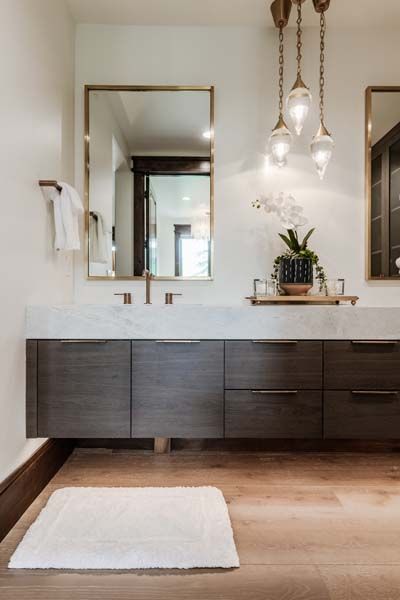 Modern bathroom with dark wood vanity, double sinks, mirrors, pendant lights, and a white bath mat