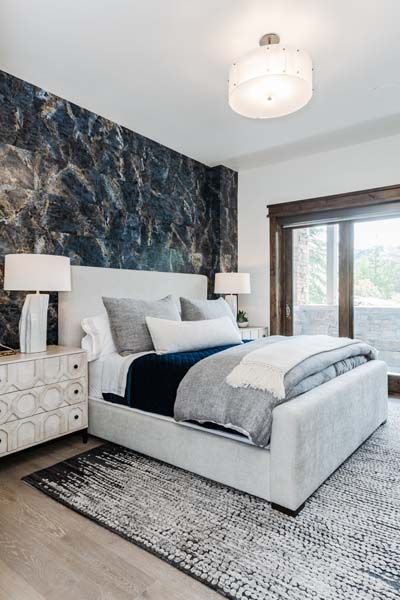 Modern bedroom with white upholstered bed, dark accent wall, patterned rug, and sliding glass doors