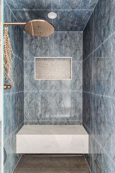 Blue-tiled shower stall with rainfall showerhead, wall niche, and bench seat.