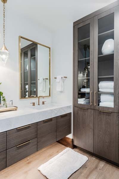 Modern bathroom with double vanity, gold-framed mirror, glass cabinet, and folded white towels.