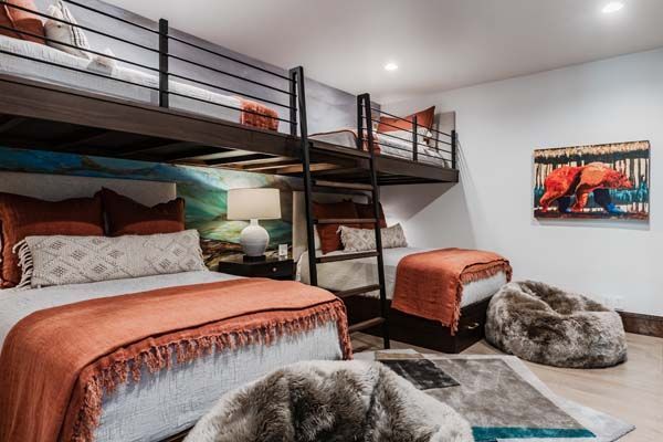 Modern bunk room with black metal beds, rust bedding, a ladder, and a furry gray chair near a painting.