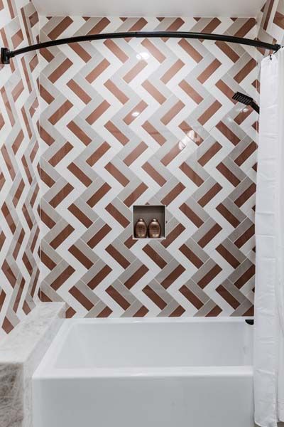 Tiled shower wall with geometric brown-and-white pattern over a white bathtub and shower curtain.
