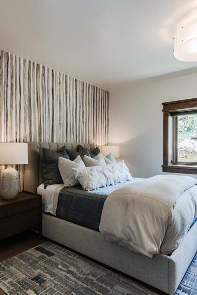 Cozy bedroom with a gray bed, striped wallpaper, bedside lamp, and window