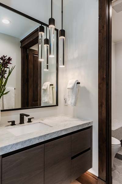 Modern bathroom vanity with large mirror, hanging pendant lights, white countertop, and dark wood cabinetry
