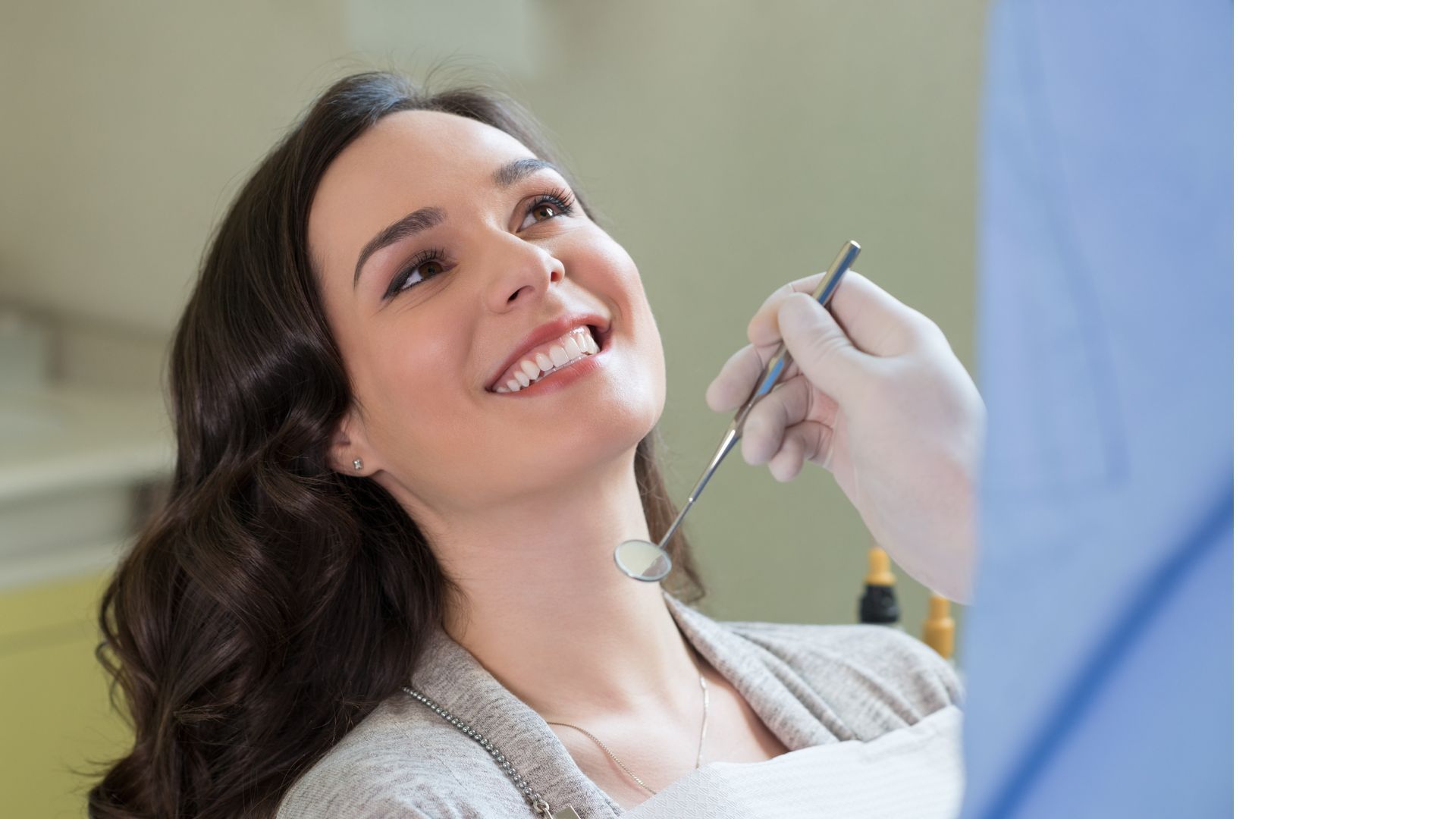Woman smiling during a dental exam; dentist holds a tool to check her teeth.