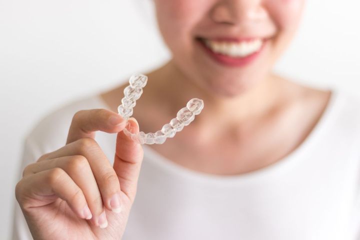 Woman holding clear aligner, smiling, white background.